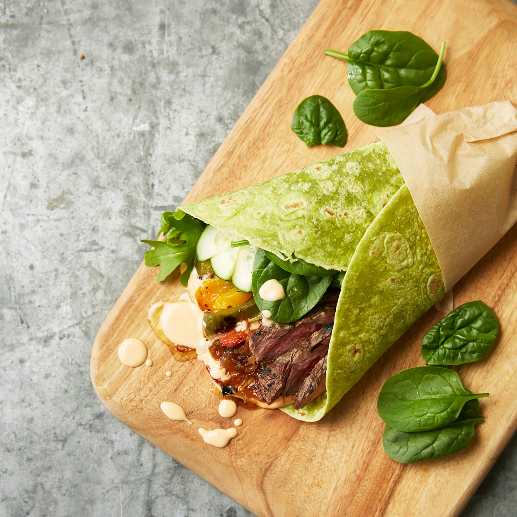 A freshly prepared wrap with leafy greens on a wooden board