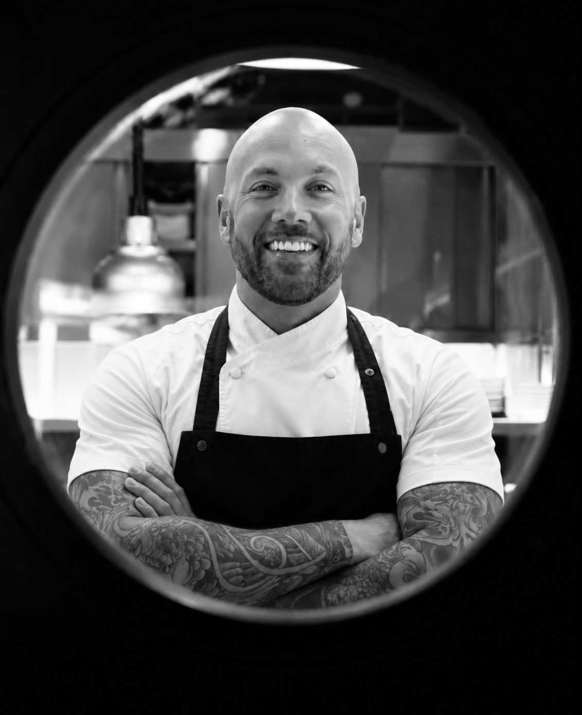 Black-and-white portrait of Daniel James in chef’s whites and an apron